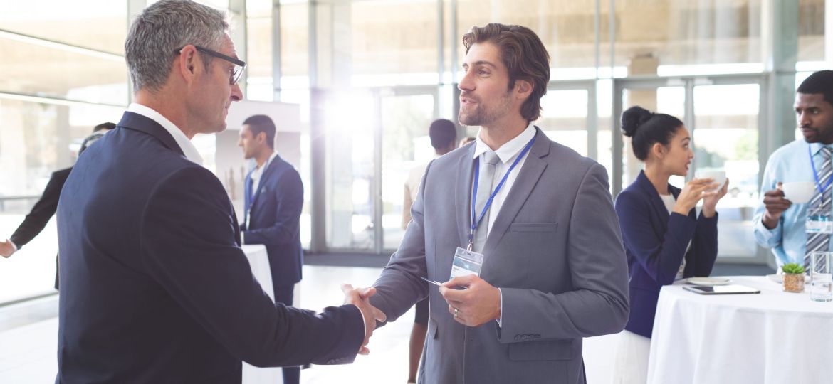 Side view of caucasian happy business people shaking hand during a seminar. Diverse business people are interacting behind them